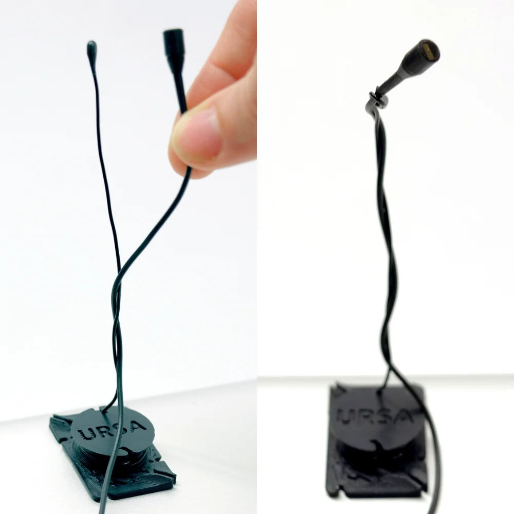 Two black URSA clip mics with thin cords, lifted and held by hands
