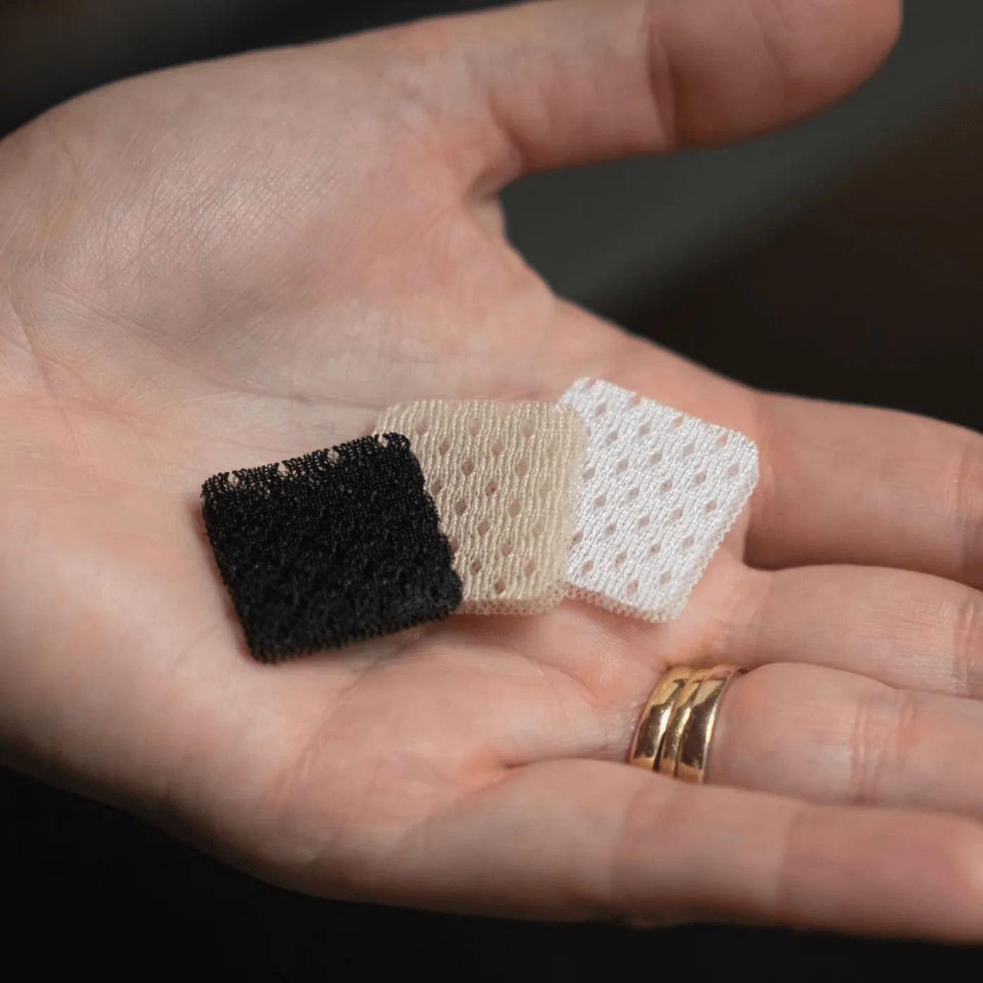 Three lav mic cover pads in hand: black, beige, and white