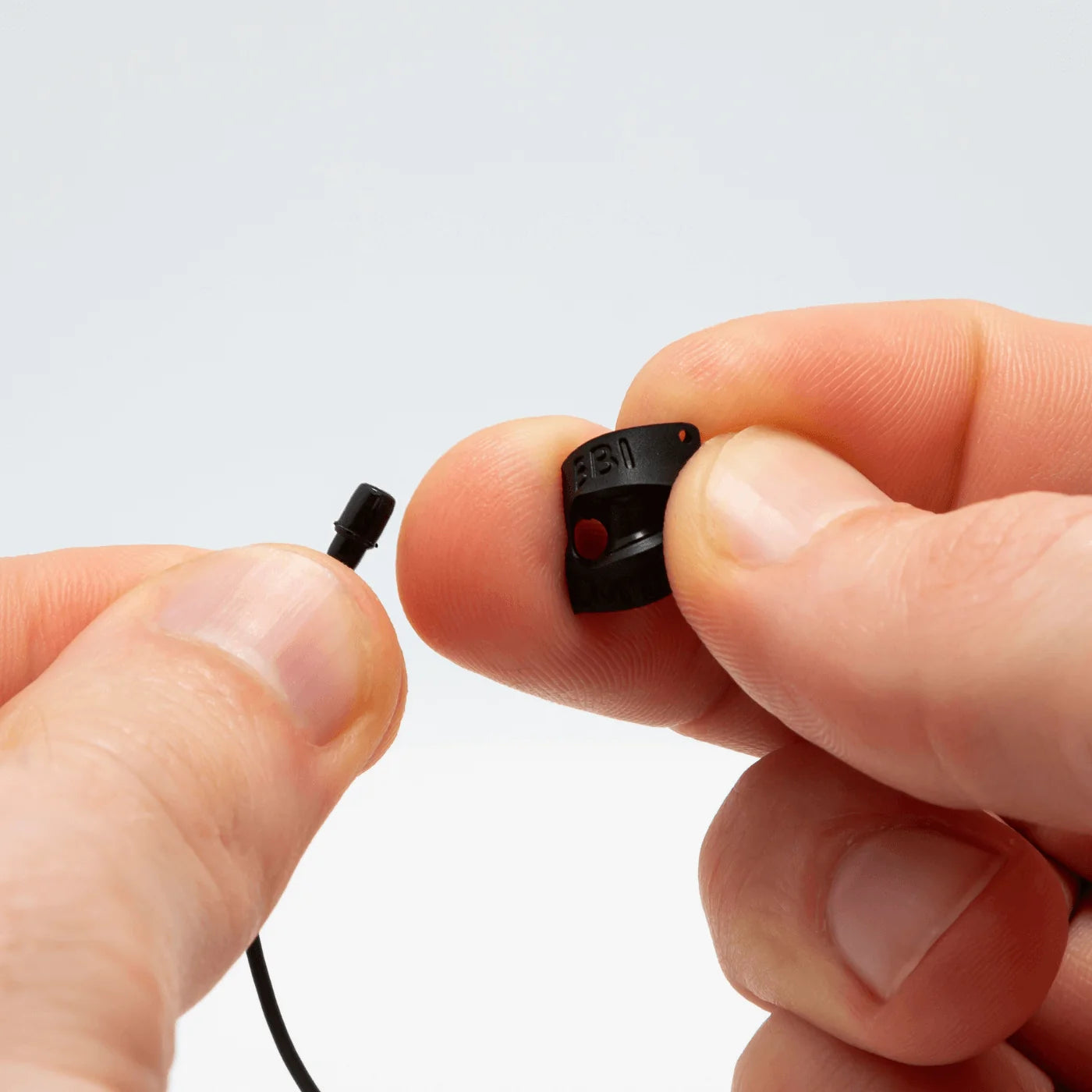 Hand holding a small black lav concealer clip with looped cable
