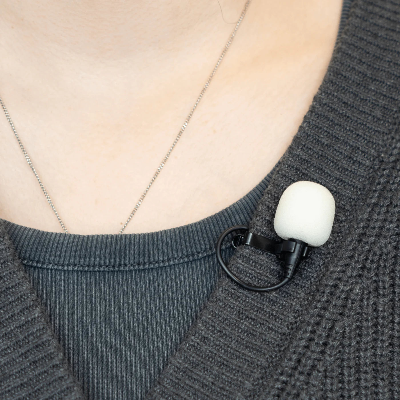 White foam windscreen on a clip-on lavalier microphone attached to dark knit