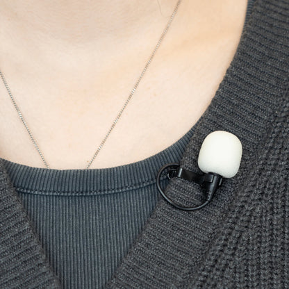 White foam windscreen on a clip-on lavalier microphone attached to dark knit