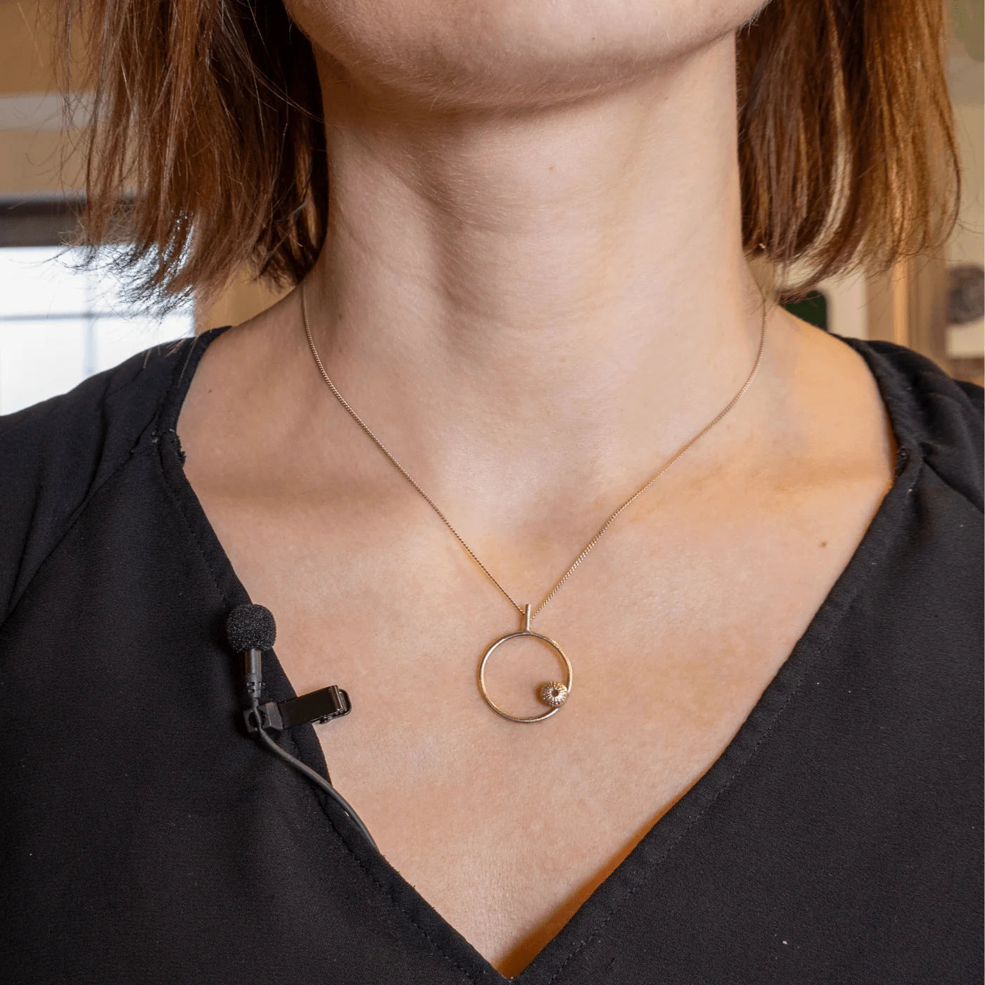 Black foam windscreen on a clip-on lavalier microphone secured near the neckline