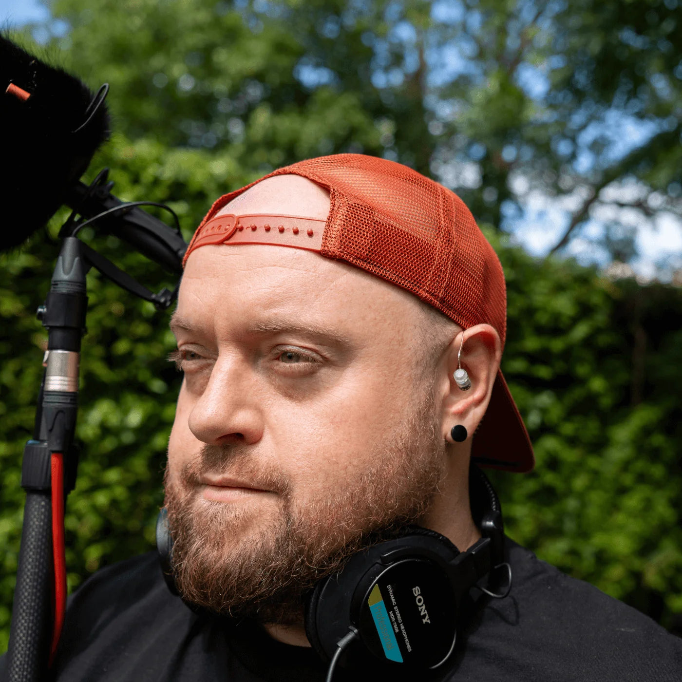 Broadcast earpiece with ear-mounted mic and black headset, worn by a man