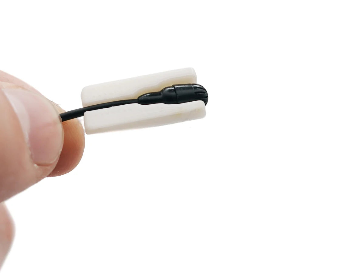White lavalier microphone windscreen mount with cable and foam cover, held by fingers