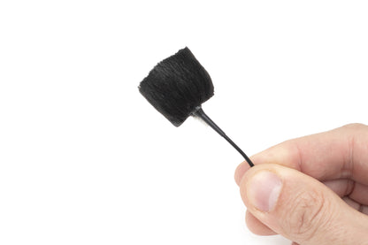 Hand holding sticker applicator with black foam brush tip on thin handle