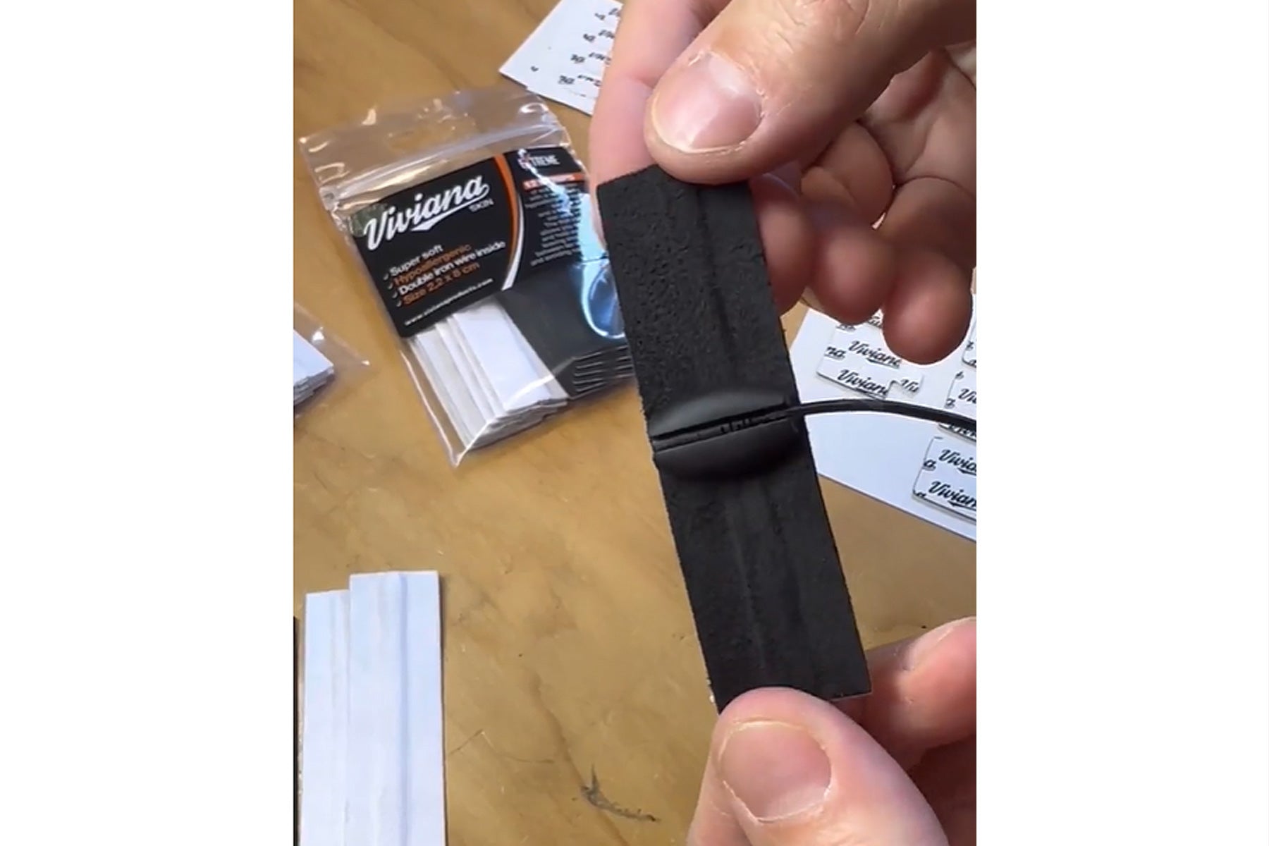 Black self-adhesive moleskin strip held between fingers