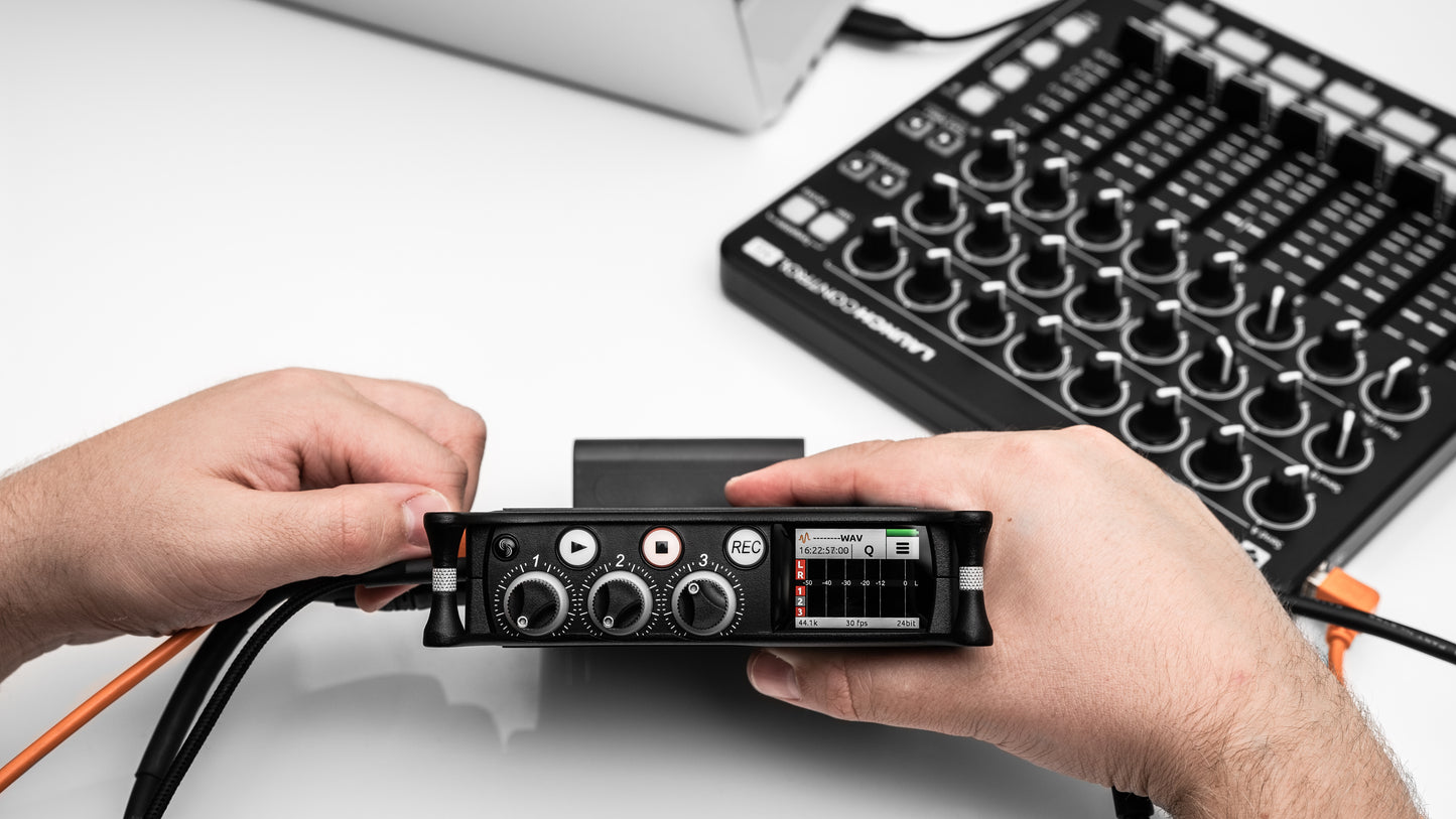 Hands holding a compact black portable audio recorder/interface with multiple input knobs.