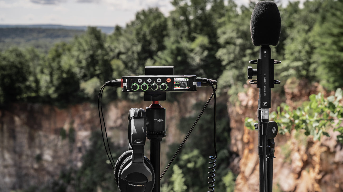 Audio mixer/preamp mounted on a stand with microphone and attached cables outdoors