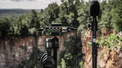 Audio mixer/preamp mounted on a stand with microphone and attached cables outdoors