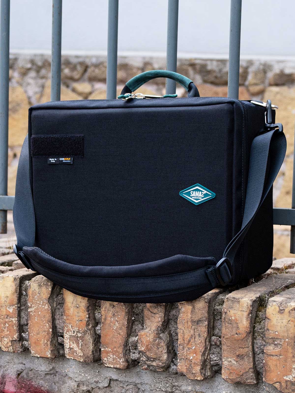 Black crossbody organizer case with teal-lined interior and front emblem patch.