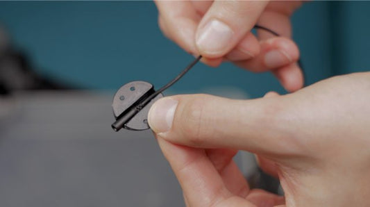 Lavalier microphone clip being attached by hand to a small base