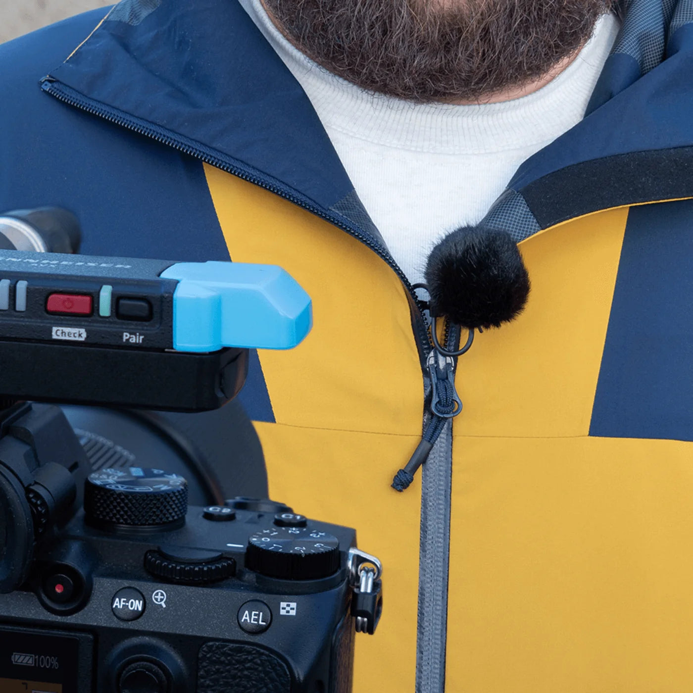 Furry windscreen pom-pom attached to a microphone on a blue and yellow jacket