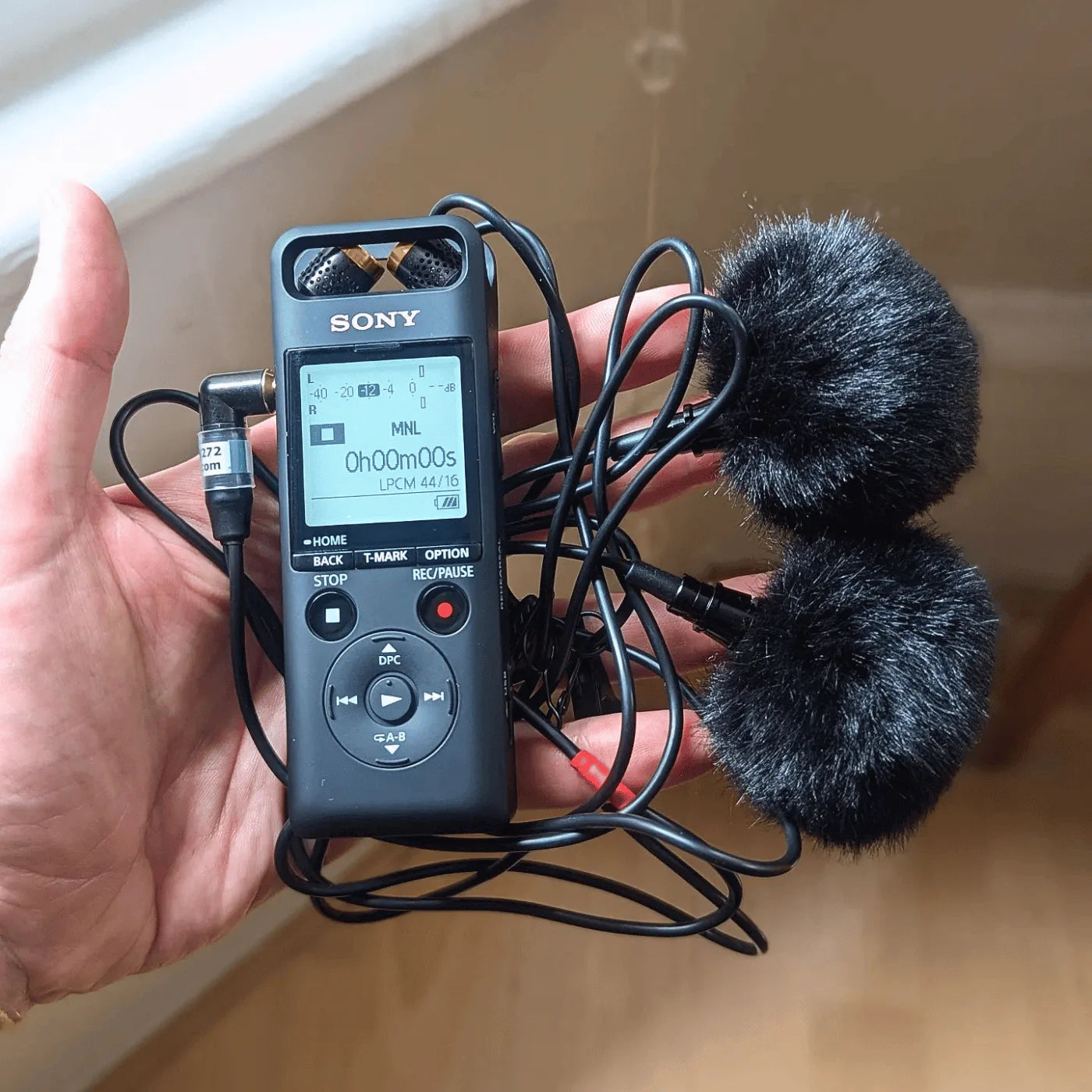 Black furry microphone windscreen cover attached to a portable recorder and cable