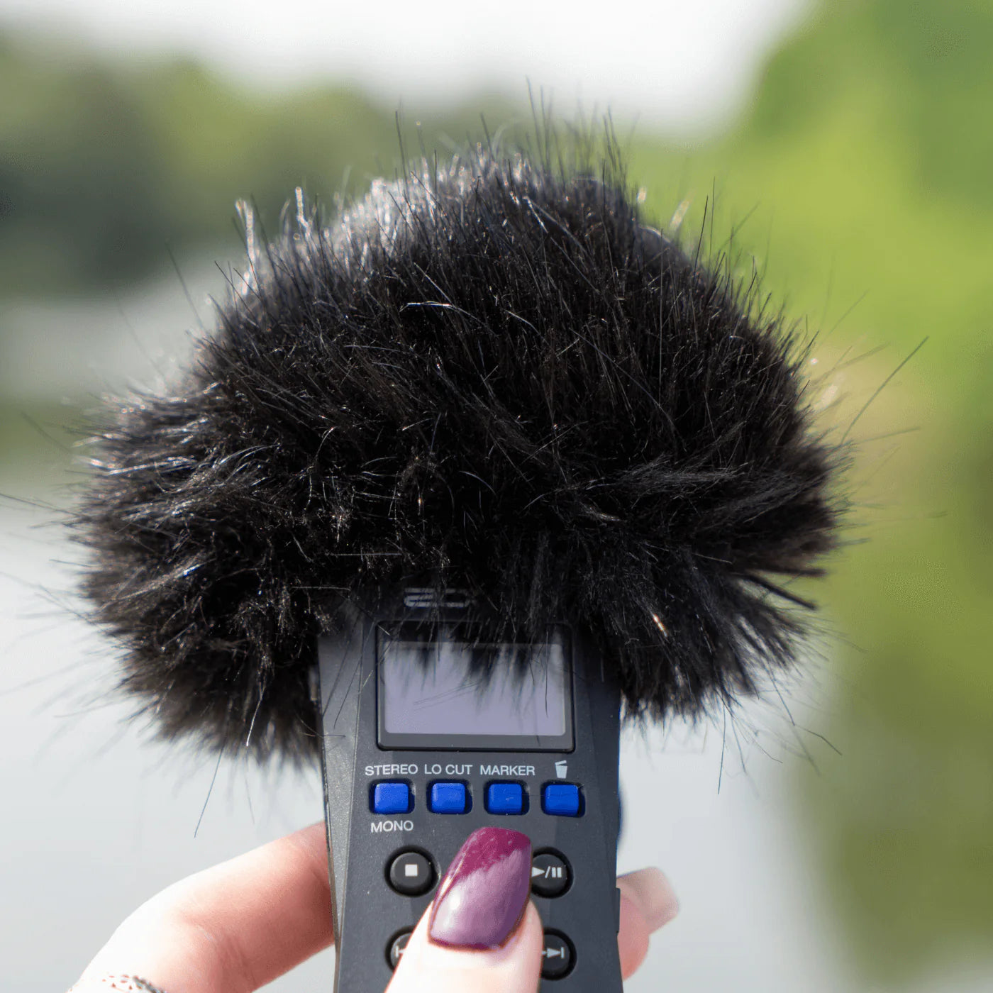 Close-up of handheld recorder with black furry windscreen and finger grip